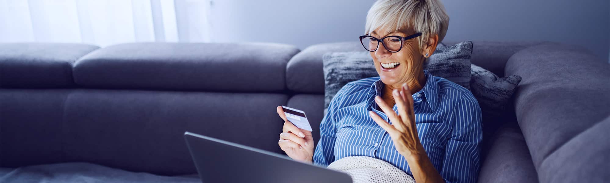 A middle-aged woman joyfully pulling out a credit card to purchase a luxury massage chair